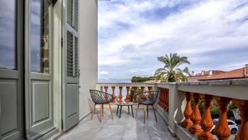 A balcony with two chairs and a small table, overlooking a cityscape with palm trees and buildings.