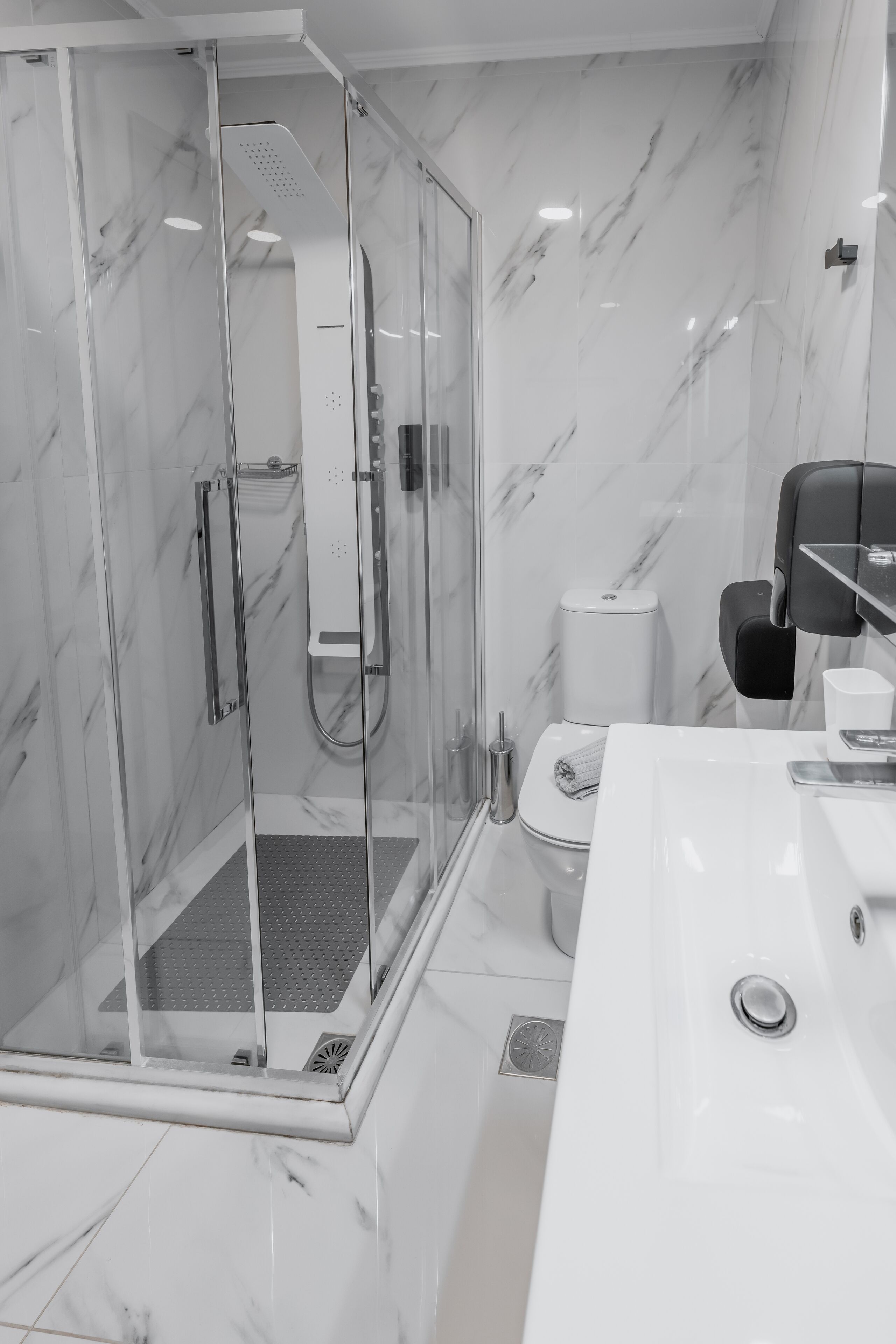 Un baño moderno con ducha de vidrio, un lavamanos blanco y un inodoro.