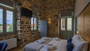 Een slaapkamer met stenen muren, een bed met handdoeken, een kledingkast en een aan de muur bevestigde televisie.