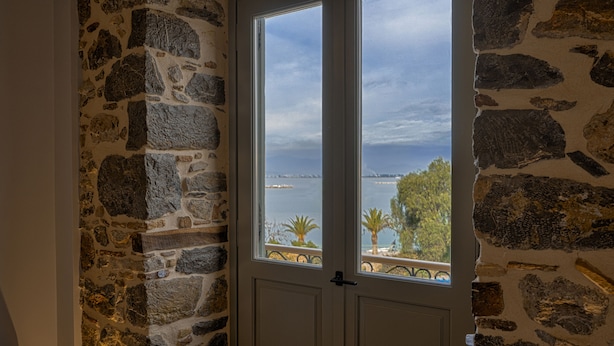 Een stenen muur met een deur die leidt naar een balkon met uitzicht op zee en palmbomen.