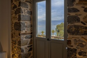 A stone wall with a door leading to a balcony with a view of the sea and palm trees. - Impero Nafplio Hotel & Suites (Nafplio)