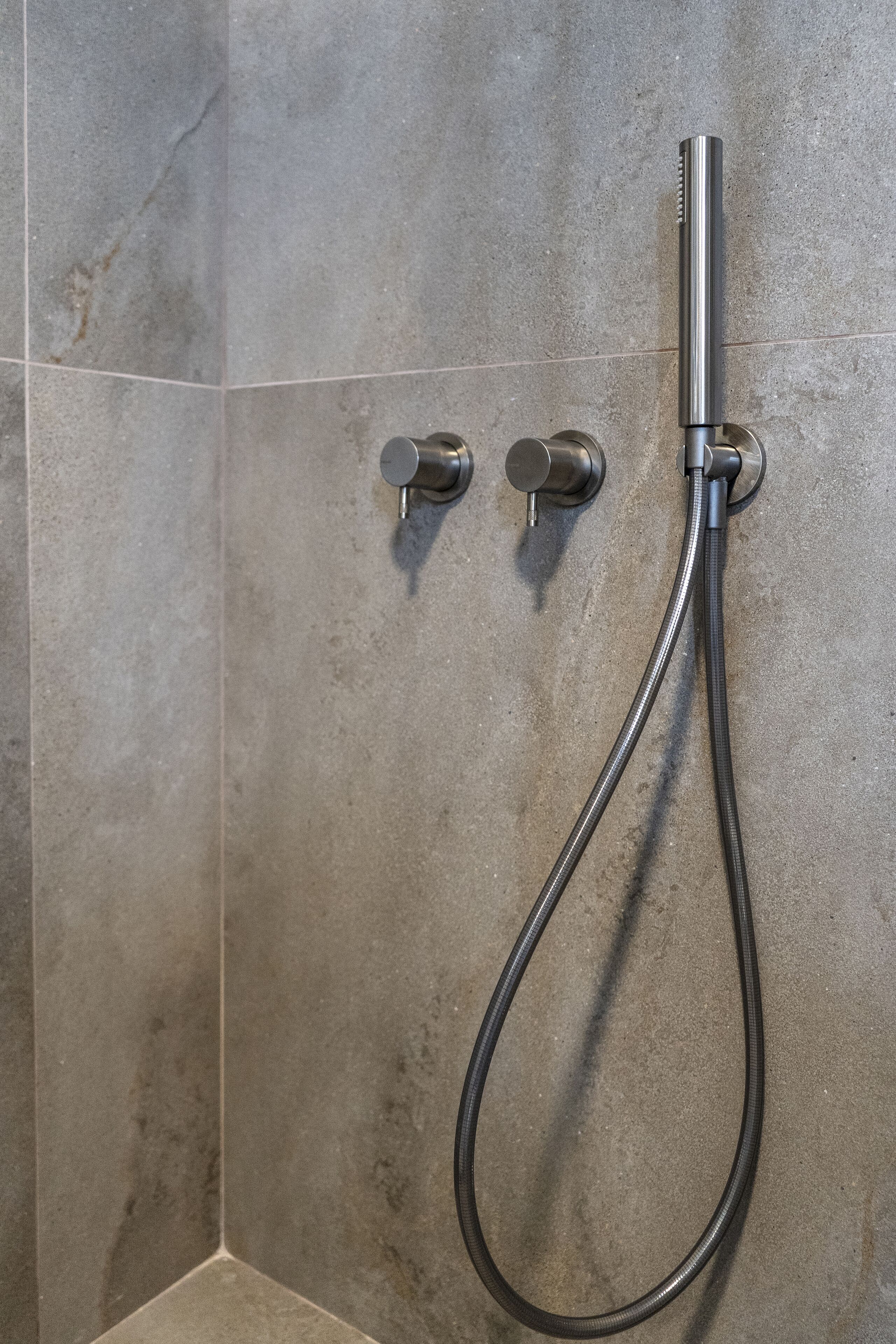 A shower with a flexible hose and two control knobs on a tiled wall.