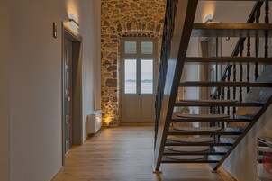 Una escalera con pared de piedra, suelo de madera y vista al mar a través de una puerta.