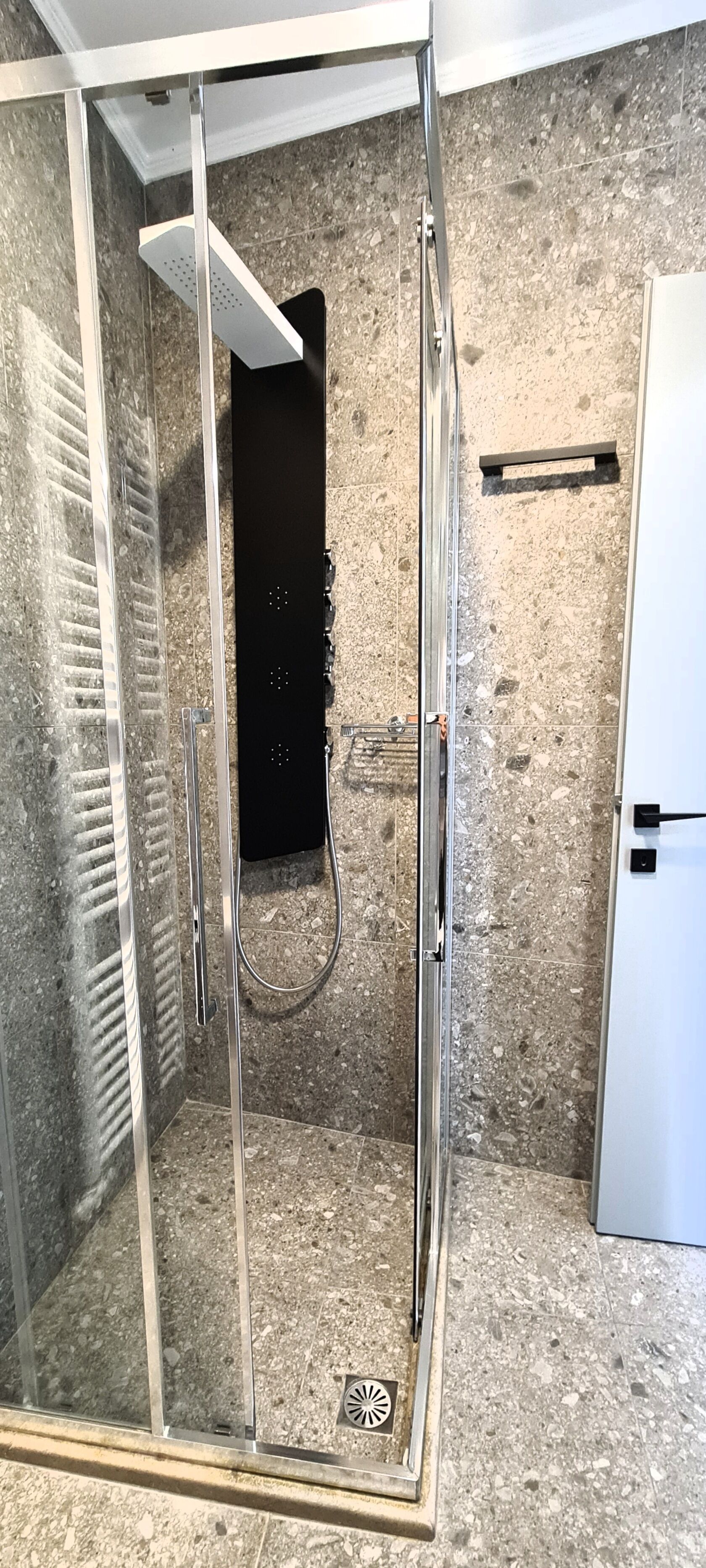A shower with a glass door, a metal handle, and a showerhead.