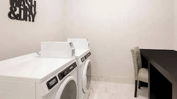 Ein Waschraum mit einer Maytag Waschmaschine und einem Trockner, einem Schild mit der Aufschrift 'WASH & DRY' und einem dunklen Holztisch mit einem Stuhl.