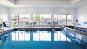 A swimming pool with clear blue water, a diving board, and a seating area with chairs and tables.