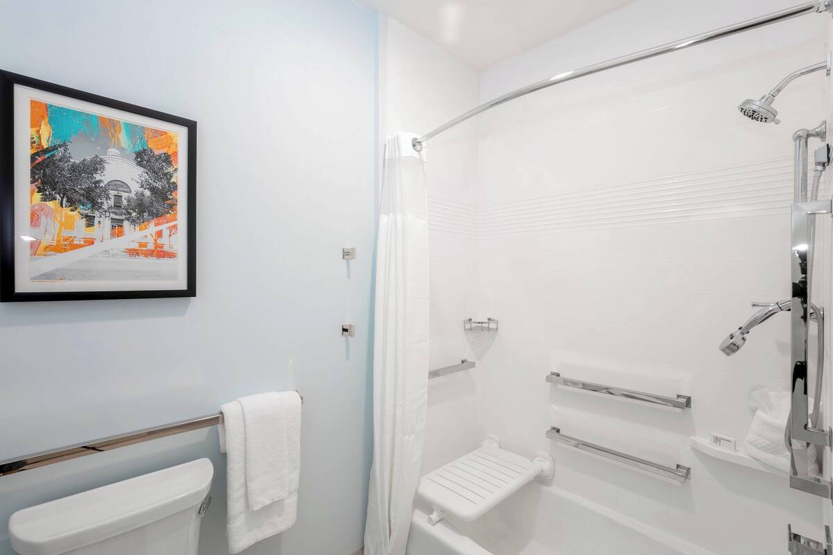 Un baño con inodoro, ducha con puerta de cristal, un cuadro en la pared y un perchero para toallas.