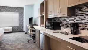 A modern hotel room with a kitchenette, a bed, a desk, and a large window.