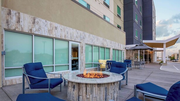 An outdoor seating area with a fire pit, lounge chairs, and a building with large windows and a covered patio.
