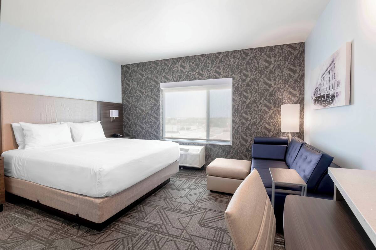 Habitación de hotel con una cama grande, un sofá, una mesita y una ventana con vistas a la ciudad.