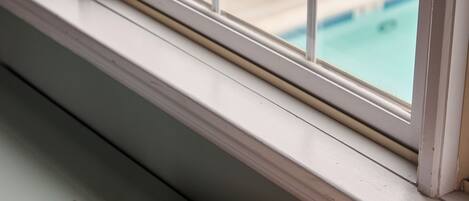 A window with a view of a swimming pool and outdoor furniture.