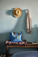 Una habitación con una cama, un banco de madera, un bolso azul, un sombrero de paja y una toalla en la pared.