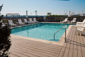 A swimming pool with a wooden deck, lounge chairs, and a fence. - The Harbor Front Inn (Greenport)