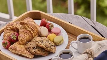 A wooden tray with pastries, cookies, macarons, strawberries, and coffee cups on a balcony.