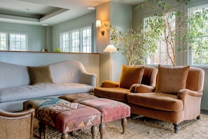Relax in this inviting living space with a sofa, chair, and ottoman, surrounded by a potted plant and natural light.