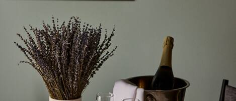 A table with a vase of dried flowers, a bottle of champagne, and two glasses.