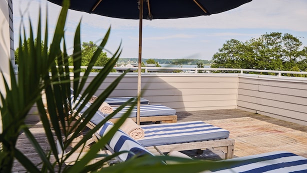 A rooftop terrace with lounge chairs, a wooden table, and a view of the landscape. - The Harbor Front Inn (Greenport)