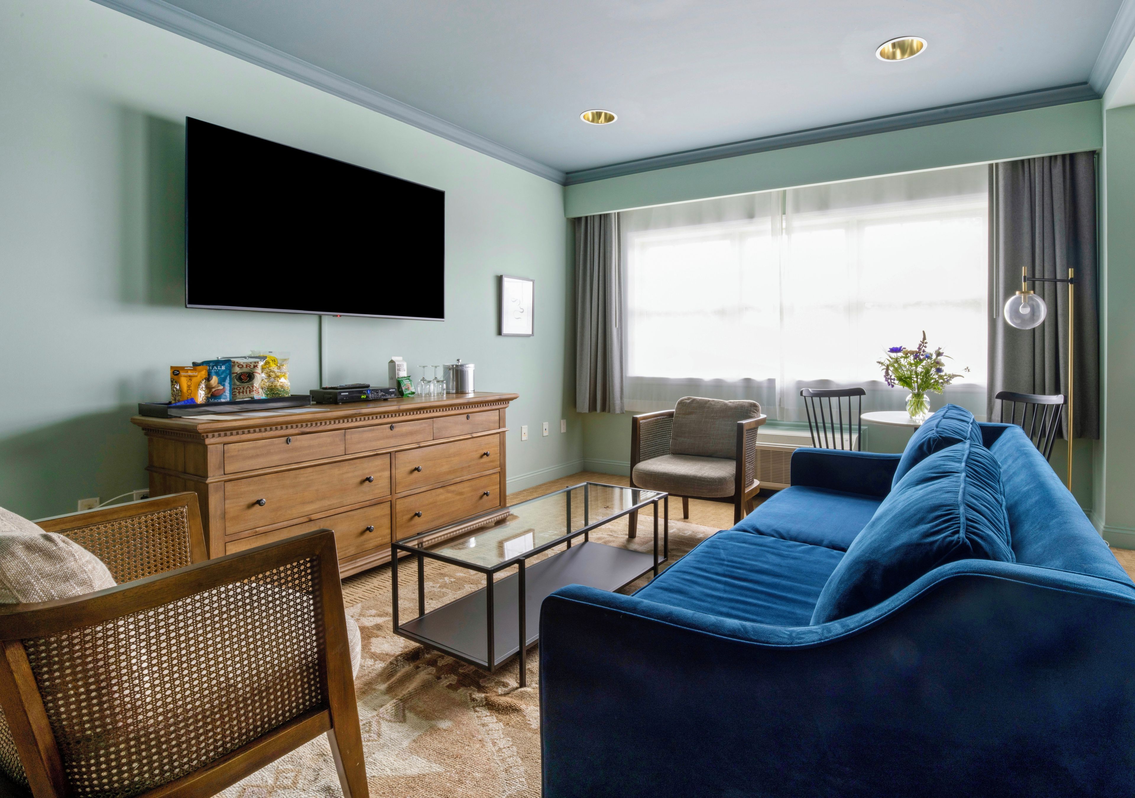 A living room with a flat-screen TV, wooden dresser, blue sofa, and a dining area with a table and chairs.