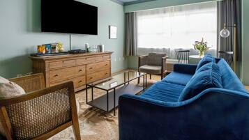 A living room with a flat-screen TV, wooden dresser, blue sofa, and a dining area with a table and chairs.