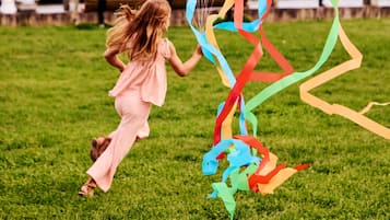 Uma criança brincando com uma pipa colorida em um campo gramado.