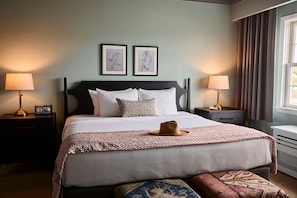 Una habitación de hotel ordenada con una cama, dos mesitas de noche con lámparas, un ventanal con cortinas y dos cuadros enmarcados en la pared.