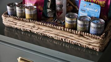 Una cesta tejida con varias latas de bebidas y paquetes de comida sobre una mesa.