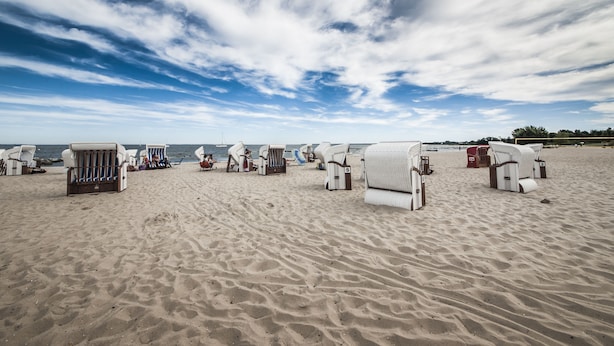 A beach with rows of white beach chairs and sun loungers, some with umbrellas.