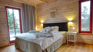 A wooden cabin bedroom with a bed, bedside table, and a window with a view of trees.
