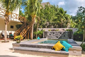 Zona de piscina con muro de piedra, palmeras y escalera de madera.