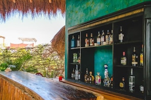 A bar area with shelves of liquor bottles, a thatched roof, and tropical plants. - Hotel Boutique La Puerta Azul Beachfront - Adults Only (Isla Holbox)