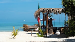 A beach scene with a thatched structure, wooden furniture, and a flag. - Hotel Boutique La Puerta Azul Beachfront - Adults Only (Isla Holbox)