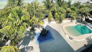 A beach view with a pool, palm trees, and a thatched roof structure. - Hotel Boutique La Puerta Azul Beachfront - Adults Only (Isla Holbox)