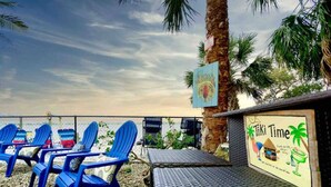 Ein Sitzbereich direkt am Strand mit blauen Stühlen, einem Tisch, Palmen und einem Schild mit der Aufschrift 'Tiki Time'.