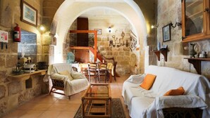 A cozy living room with a stone archway, a white sofa, a wooden coffee table, and a dining area with chairs and a table. - Charming Retreat: experience rustic elegance in this beautifully converted fh. (Santa Lucija)