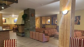 Un salon confortable avec des canapés à rayures, un pilier en pierre, des lambris en bois et une cheminée.