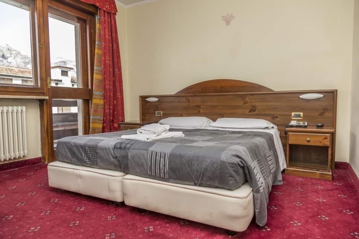 A bedroom with a double bed, two bedside tables, a window with curtains, and a radiator.