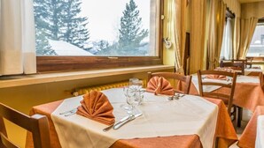 Un espace repas avec des tables dressées pour deux personnes, agrémenté de nappes blanches et de serviettes orange.