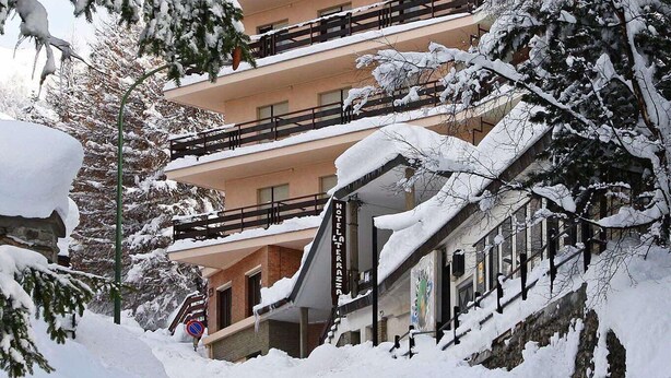 Un hôtel à plusieurs étages, doté de balcons, bordé d’arbres couverts de neige et surplombant un ciel dégagé.