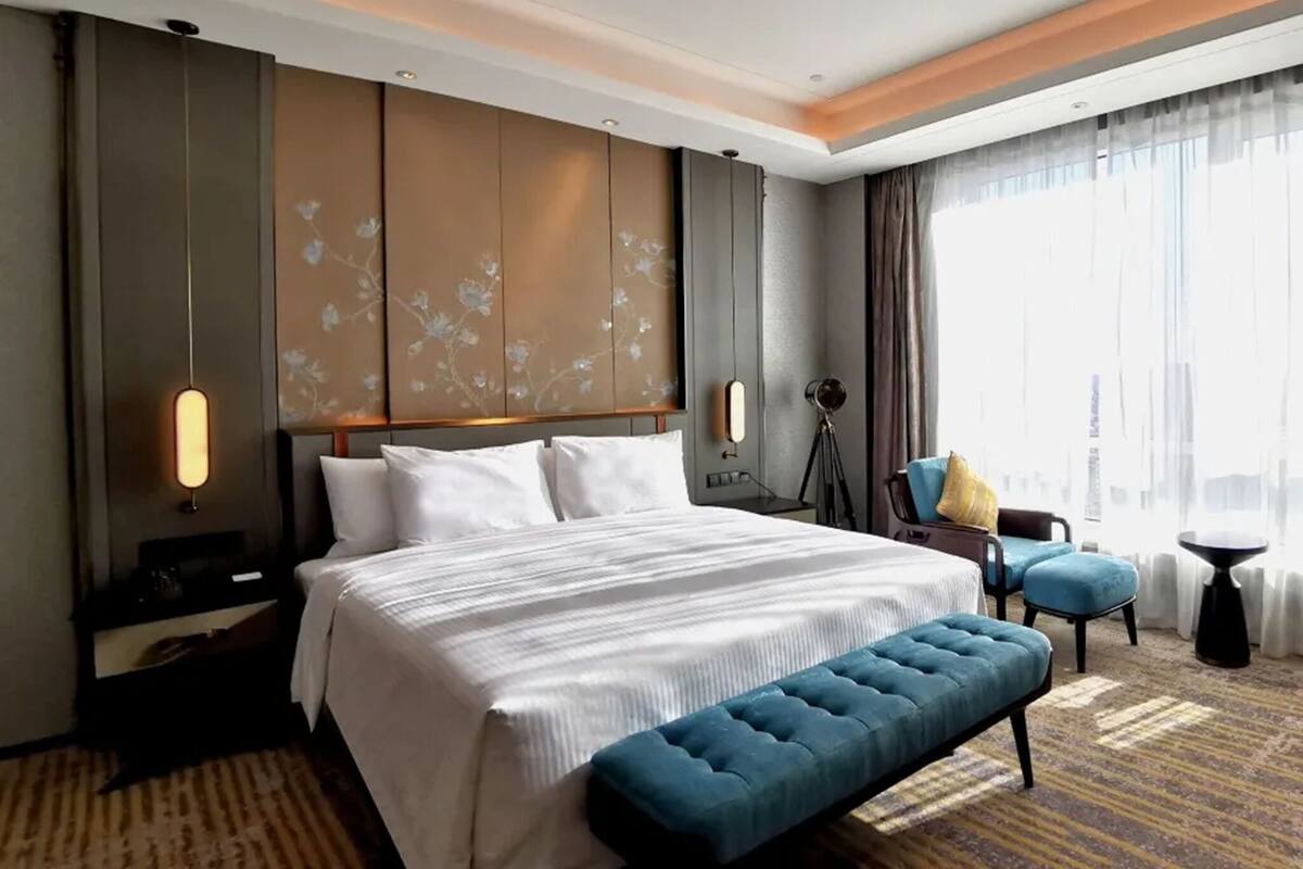 A hotel room with a large bed, a bench, a desk, and a chair.