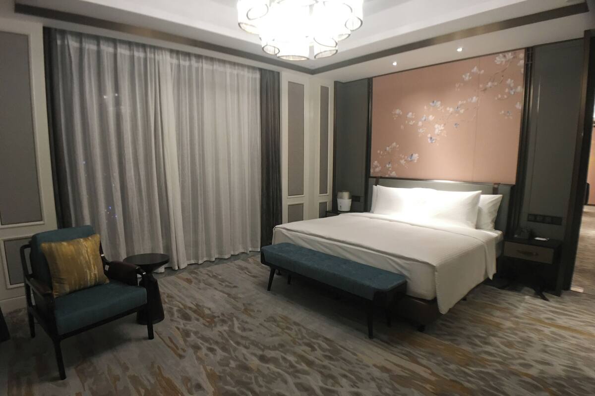 A hotel room with a large bed, a bench, a chair, and a nightstand.
