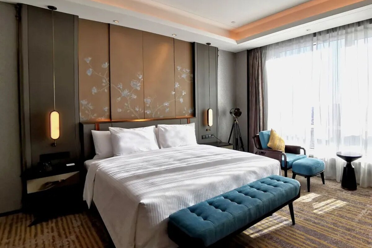 A hotel room with a large bed, a bench, a desk, and a chair.