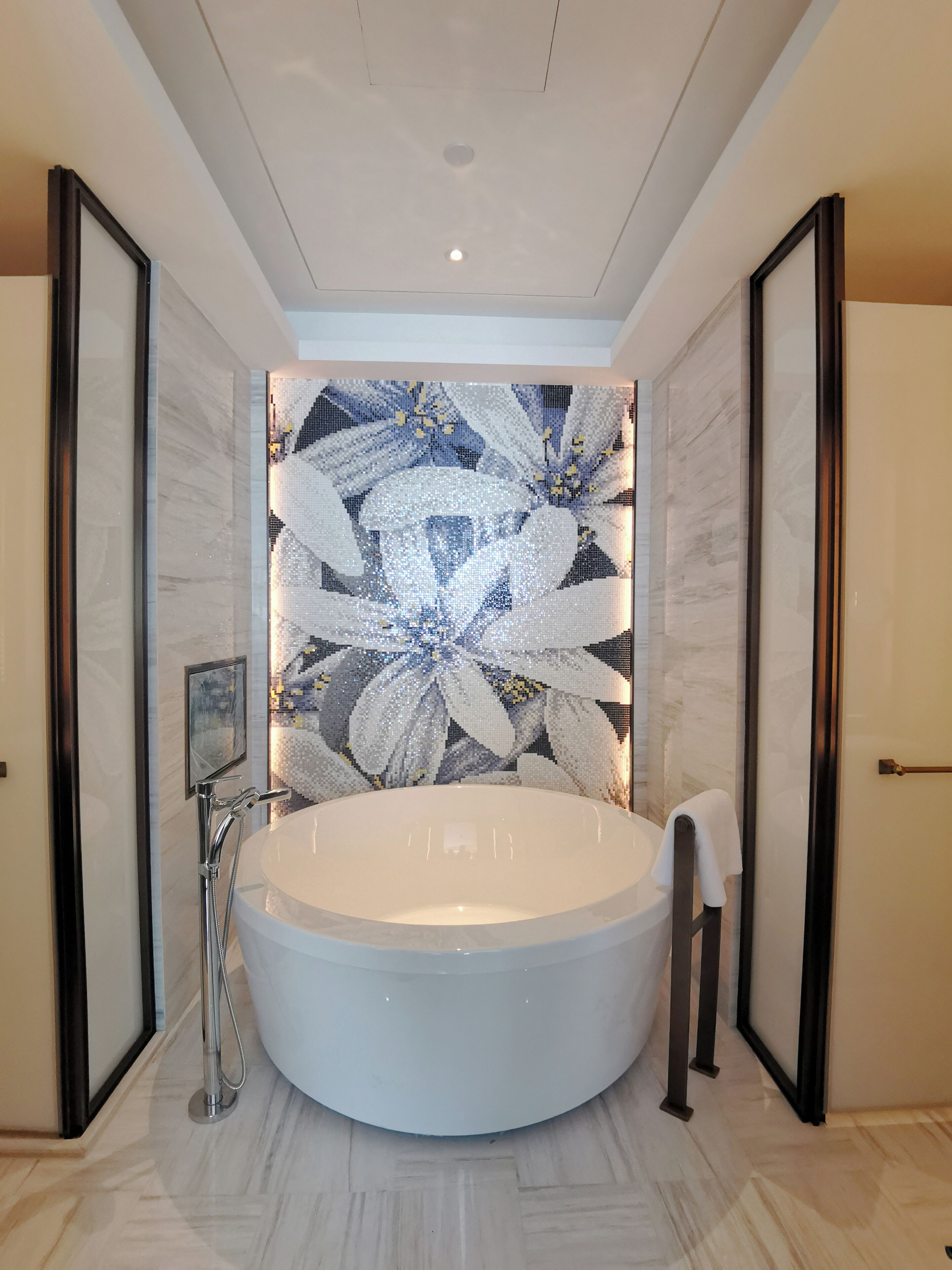 Une salle de bain moderne dotée d’une grande baignoire îlot, d’un espace douche et d’un mur décoratif en mosaïque.