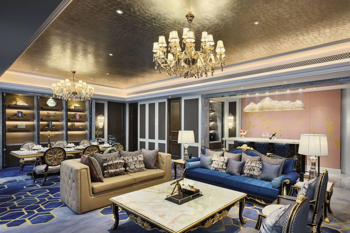 A luxurious living room with a marble coffee table, plush sofas, elegant chandeliers, and a decorative fireplace.