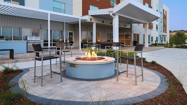 Un espace extérieur moderne aménagé avec des sièges, comprenant un foyer circulaire, entouré de chaises en métal et un patio couvert.