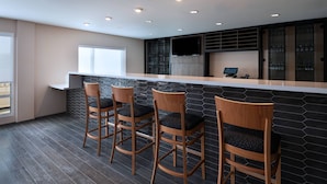 Une cuisine moderne avec un coin bar, des tabourets de bar en bois, une grande fenêtre et un téléviseur encastré.