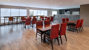 Un espace de restauration moderne avec un plancher en bois, des chaises à revêtement rouge et de grandes fenêtres qui laissent entrer la lumière naturelle.