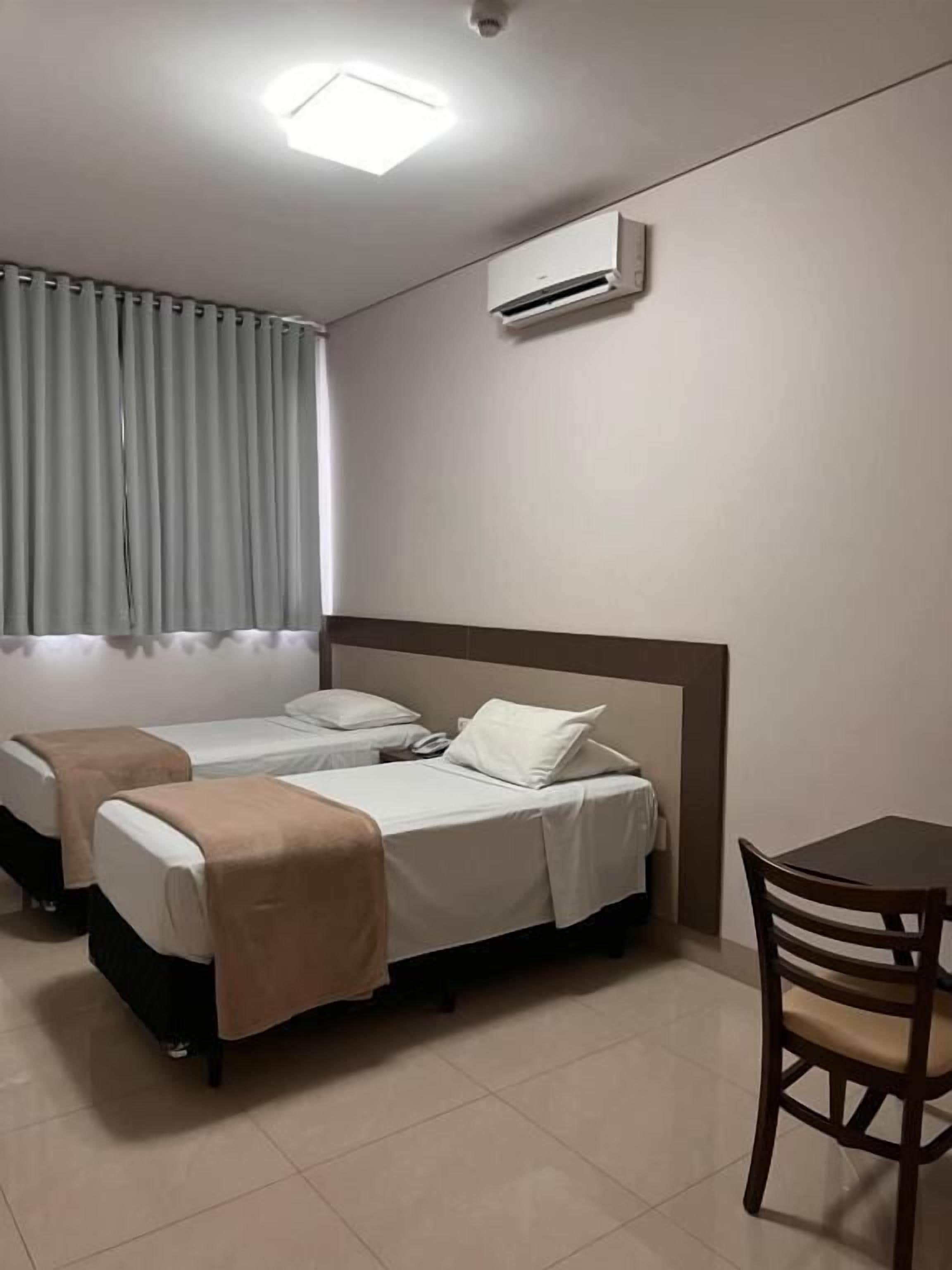 A hotel room with two beds, a table, and a chair.
