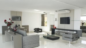 A modern living room with a grey sofa, a glass coffee table, and a flat-screen TV mounted on the wall. - Hotel Cadori (Paicandu)