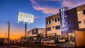 A hotel named 'Hotel Cadori' with a prominent sign, a modern building facade, and a parking area with several cars. - Hotel Cadori (Paicandu)