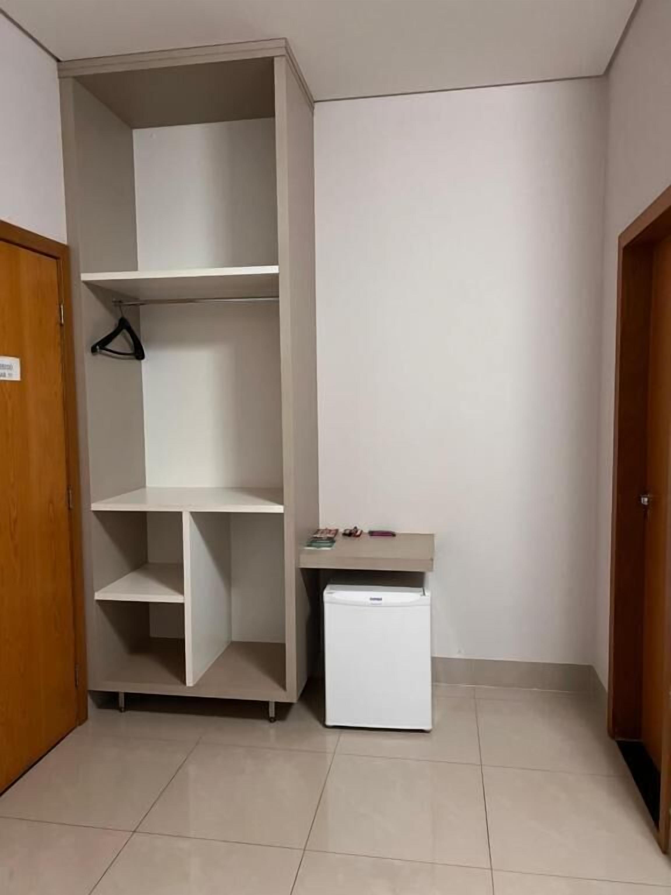 Um canto de quarto com um guarda-roupa branco, um frigorífico pequeno e branco, e uma porta de madeira.